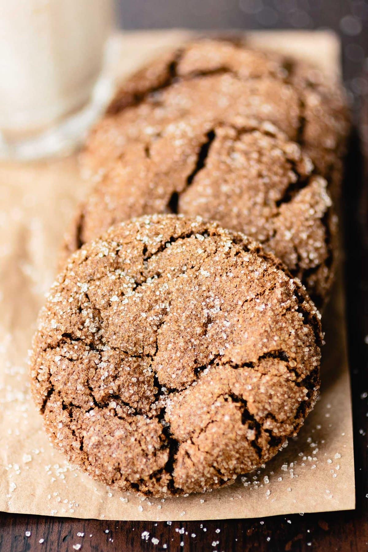 a row of crinkle-topped ginger cookies sit on a piece of parchment, sparkly with sugar sprinkles