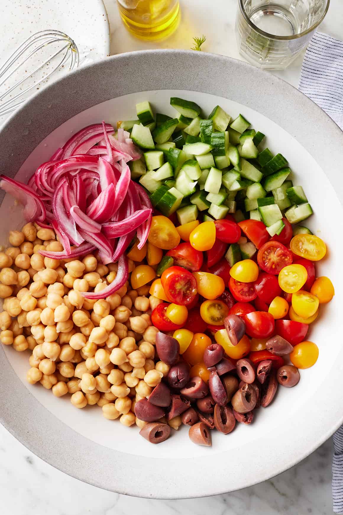 Garbanzo beans, pickled onions, cucumber, cherry tomatoes, and olives in large bowl